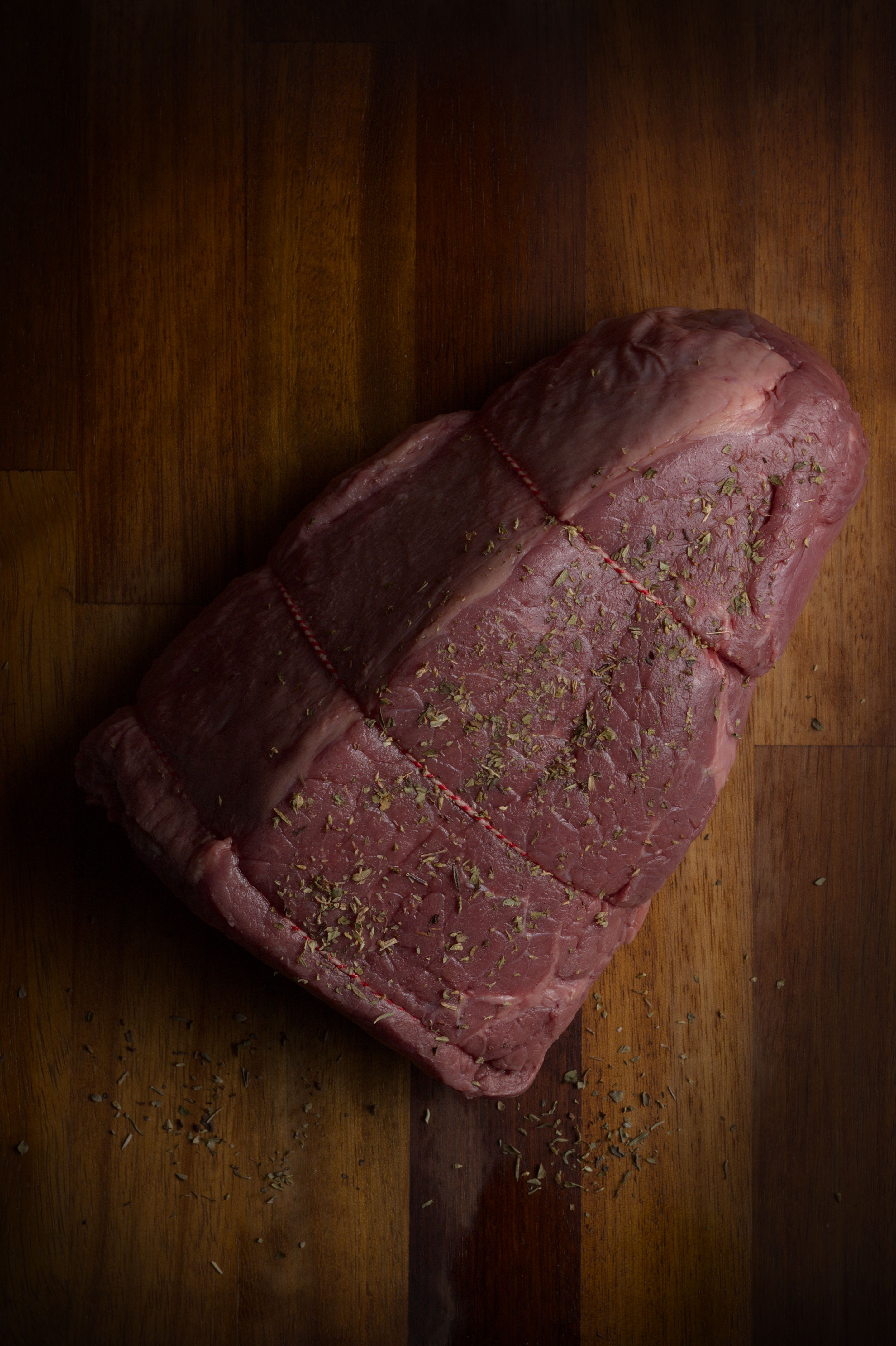 High-quality raw beef joint sprinkled with herbs on a wooden surface, perfect for cooking and culinary concepts.