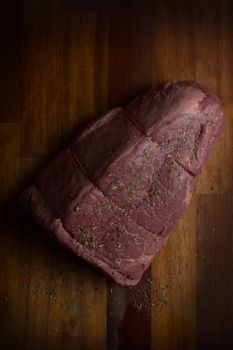 High-quality raw beef joint sprinkled with herbs on a wooden surface, perfect for cooking and culinary concepts.