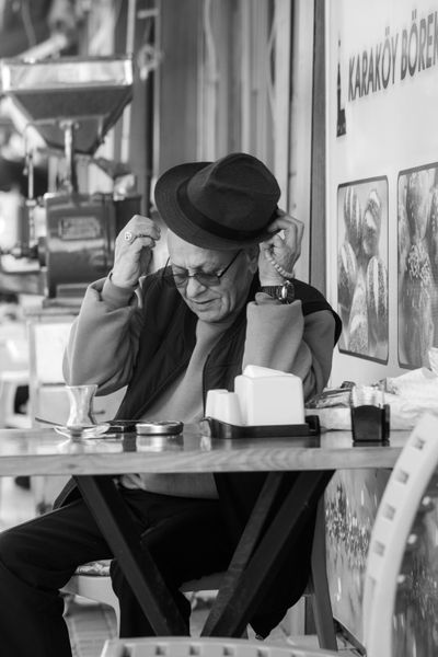 A stylish senior man adjusting his hat at a cozy street café table