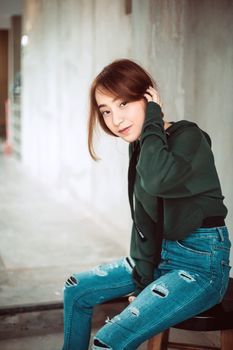 Charming Asian woman in denim and sweatshirt tucking hair behind ear looking gently at camera