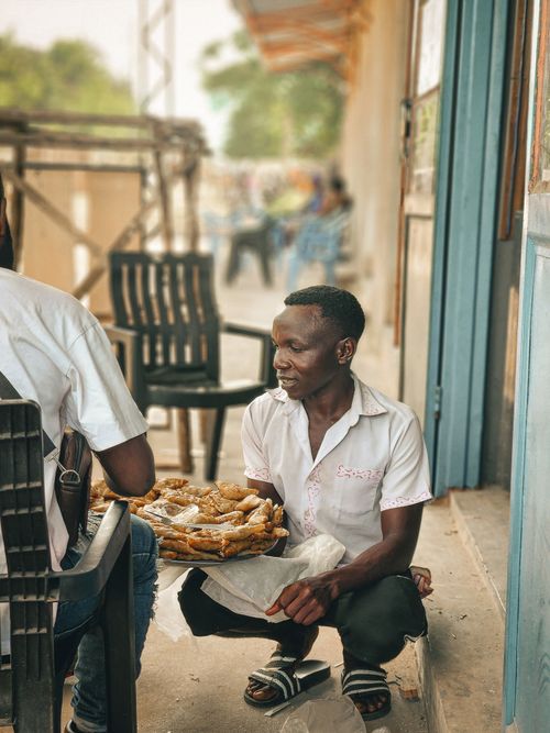 Free A man selling fried snacks to a seated customer in an outdoor setting. Stock Photo