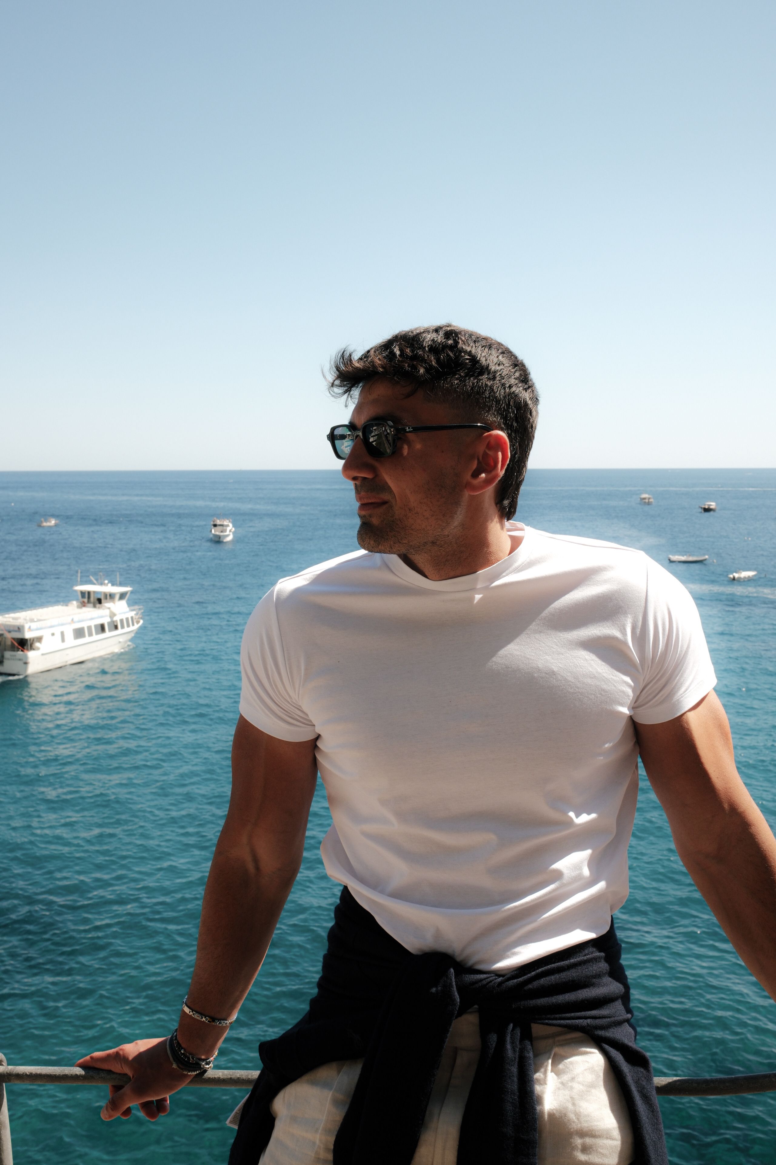 A man in sunglasses enjoys a sunny day overlooking the ocean in Positano, Italy.
