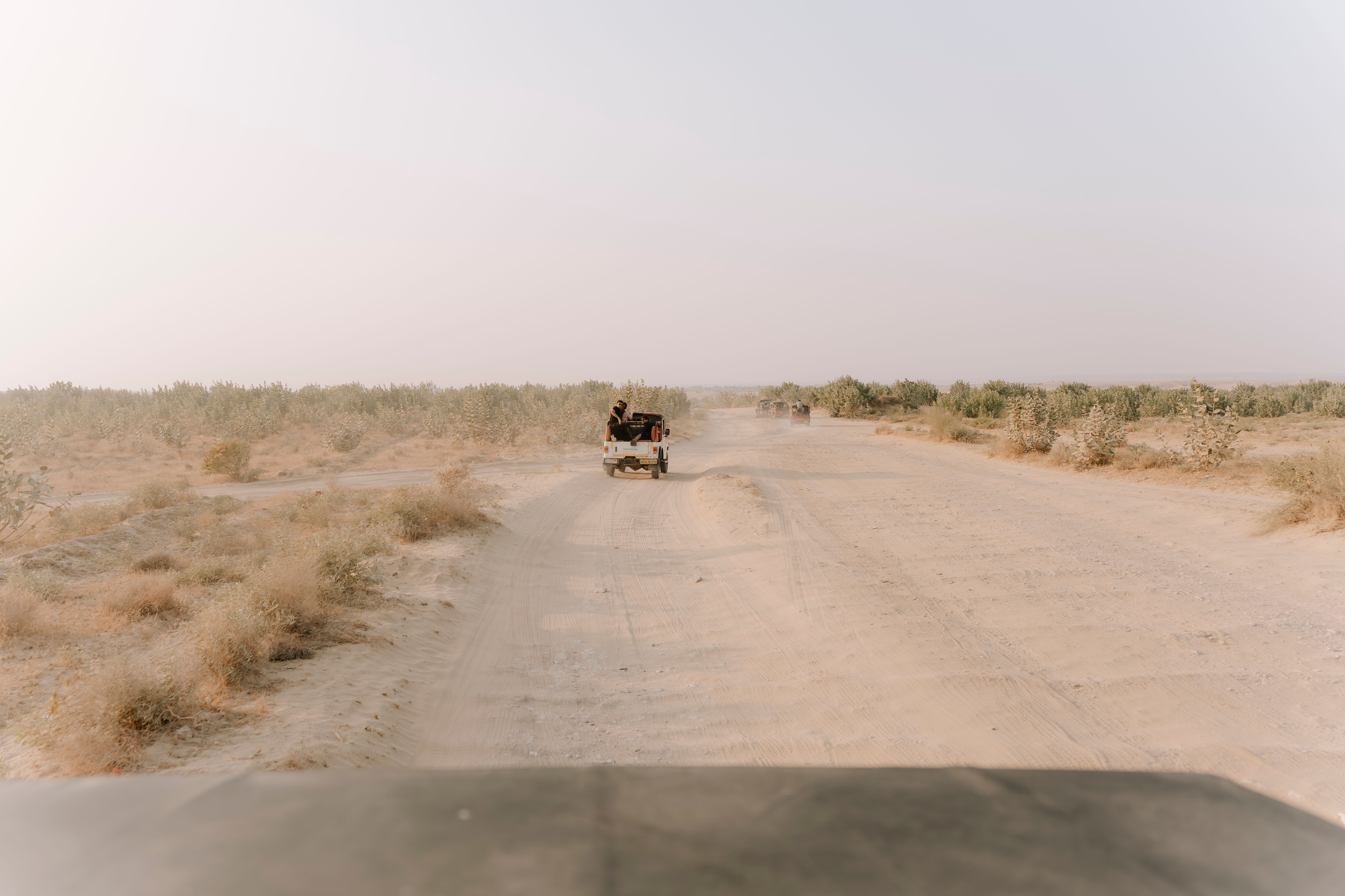A vintage jeep drives down a dusty road in the Jaisalmer desert, under a soft pastel sky.
