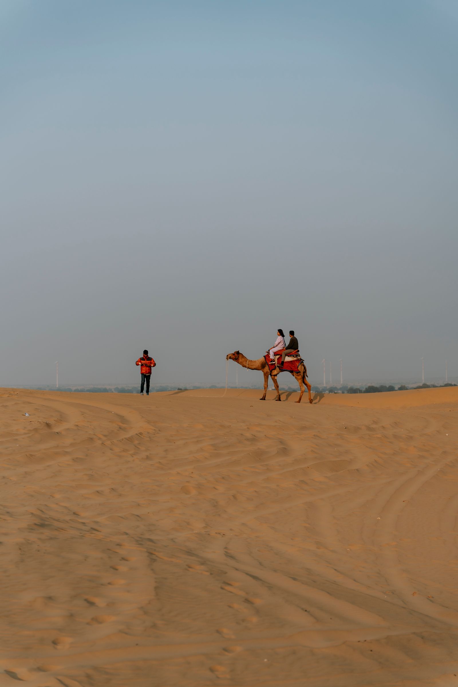 Couple riding a camel together across golden desert dunes at sunset