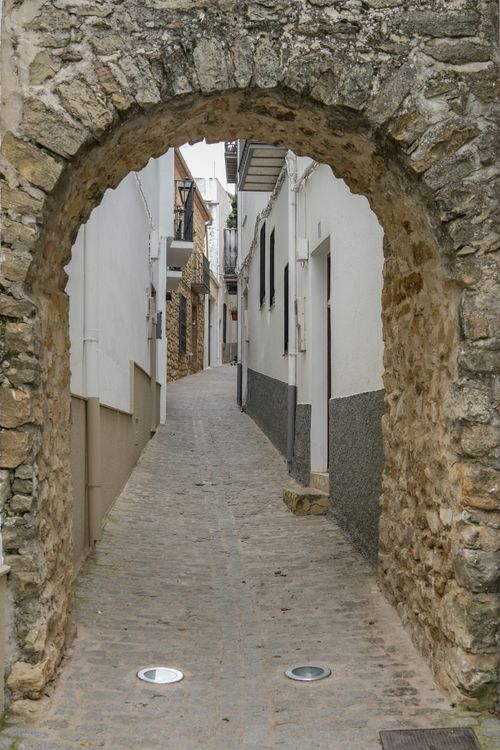 Free Cobblestone street through a rustic archway in Iznatoraf, Andalucía. Charming and historic. Stock Photo