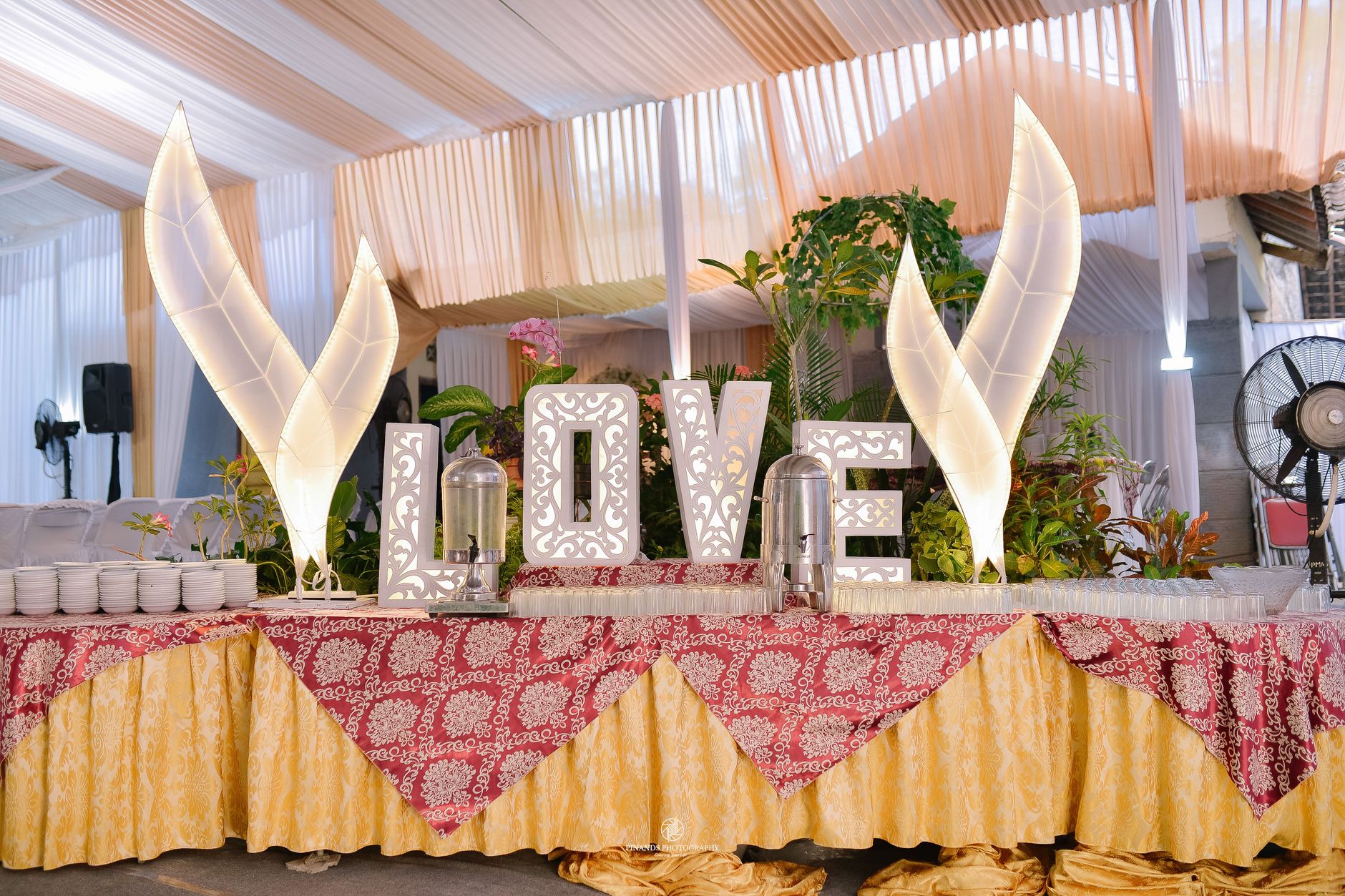 Meja prasmanan resepsi pernikahan dengan tulisan LOVE dan dekorasi bunga, sempurna untuk acara-acara elegan.