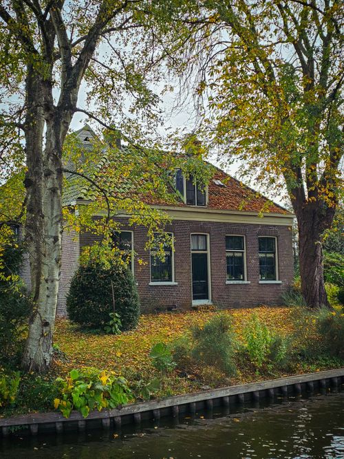 Free Quaint brick house surrounded by autumn foliage along a canal in Giethoorn, Netherlands. Stock Photo