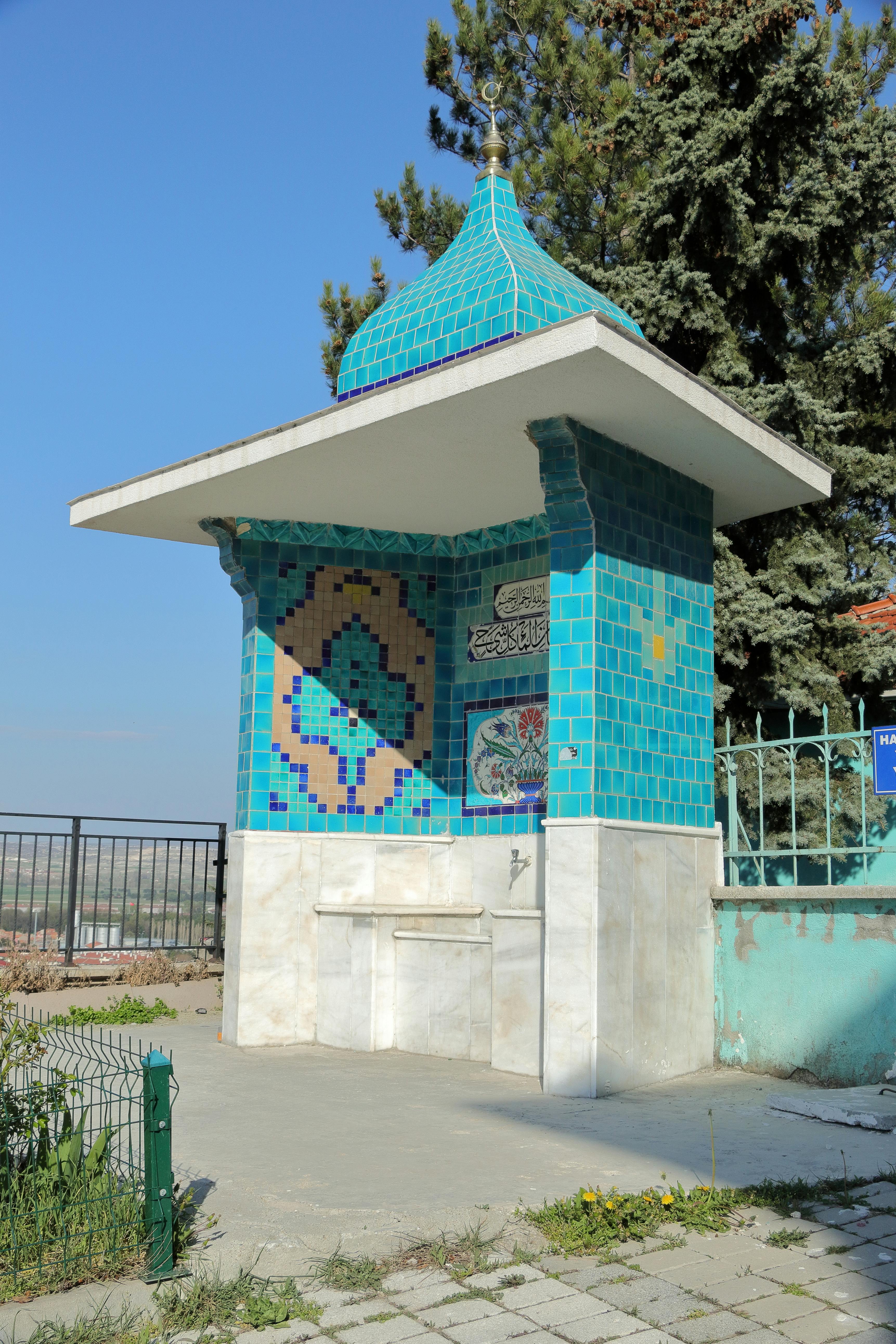 A vibrant turquoise mosaic fountain adorned with intricate patterns stands outdoors on a sunny day.
