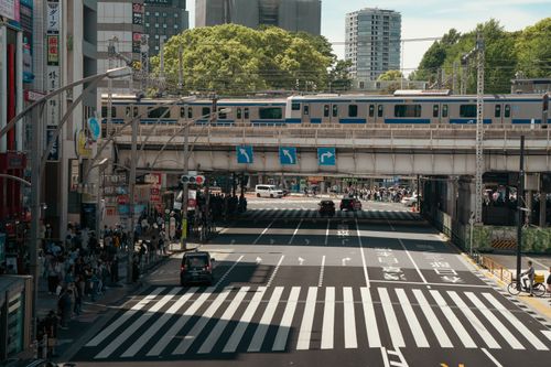 Free Tokyo cityscape featuring a busy street with pedestrians, cars, and an overhead train. Stock Photo