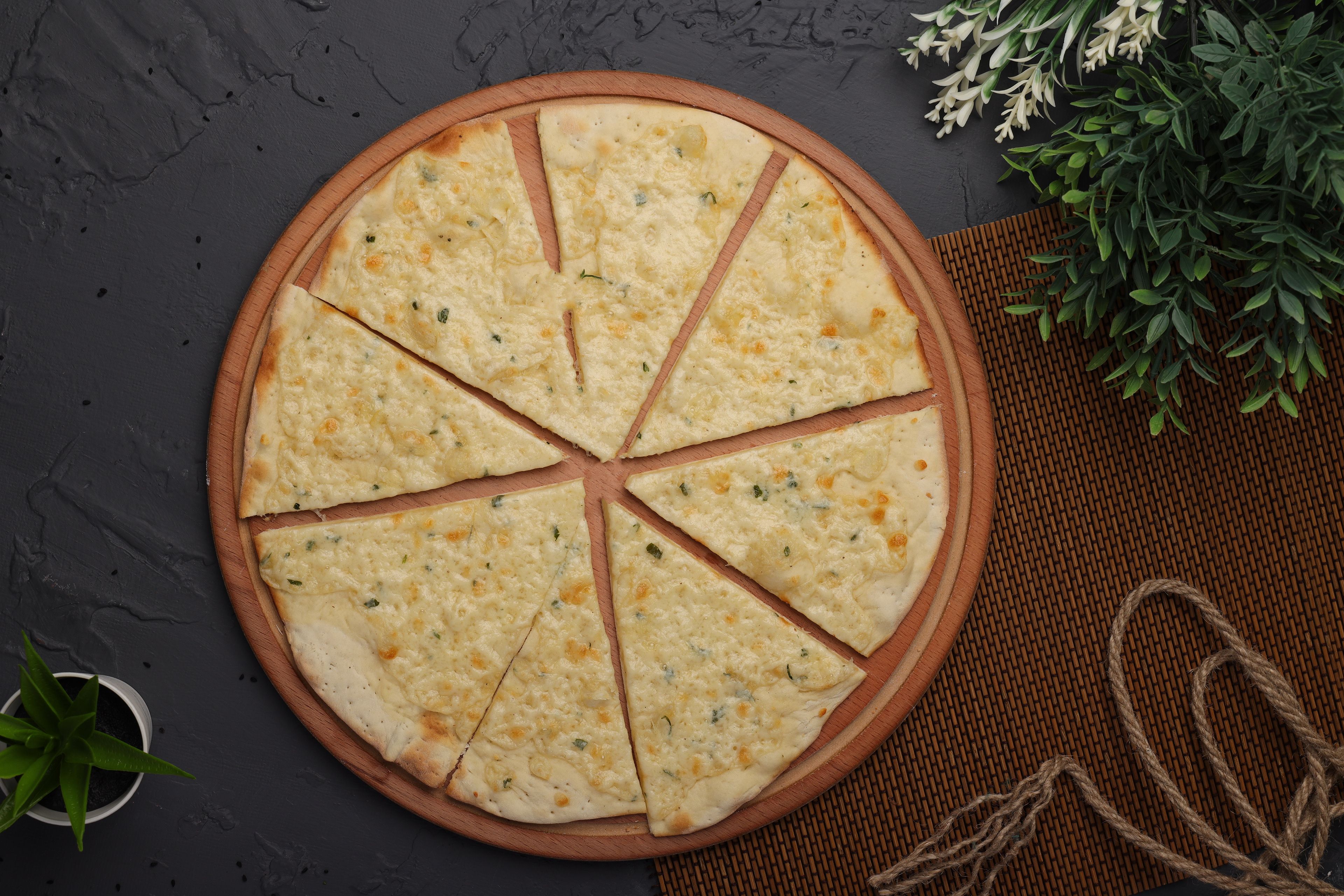 Freshly baked garlic flatbread sliced on a round wooden board with herbs.