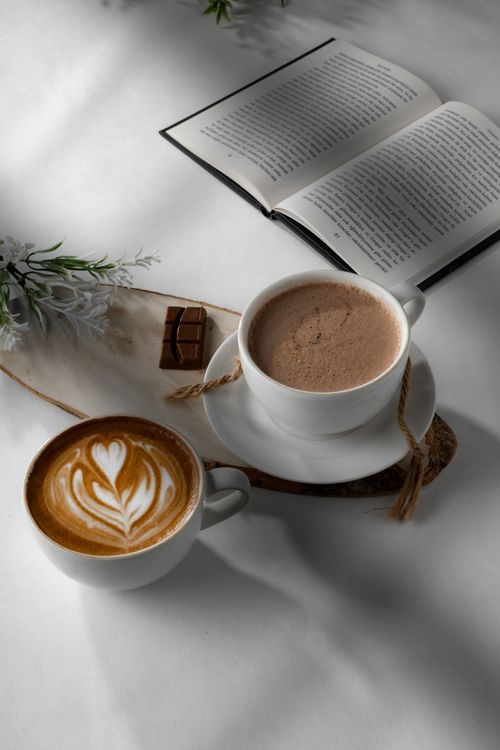 Free Warm and inviting coffee scene with latte art, open book, and chocolate on a white background. Stock Photo