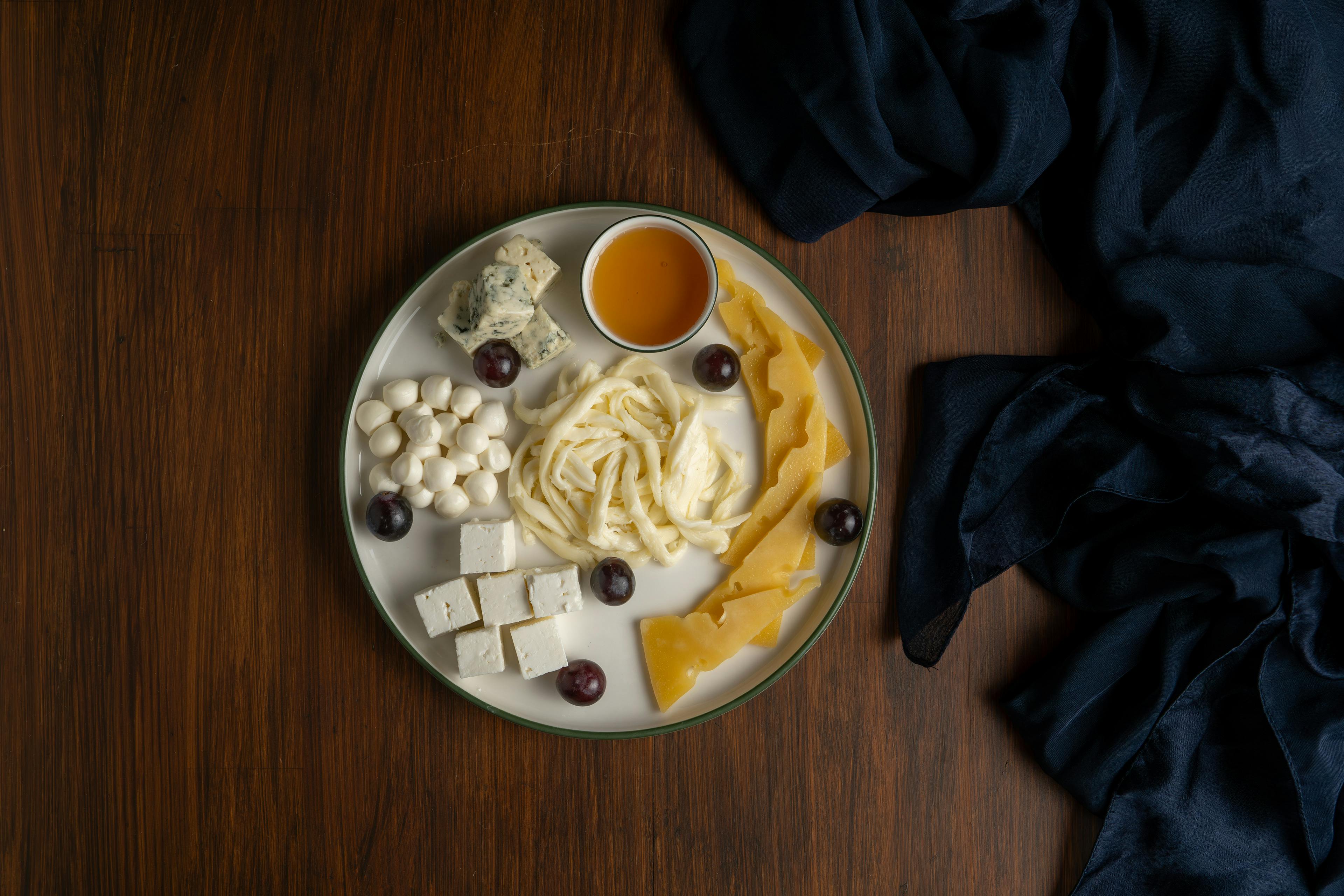 An inviting cheese platter featuring assorted cheeses, honey, and grapes on a wooden table.