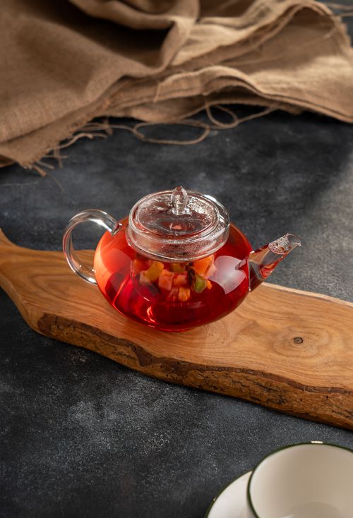 Free A glass teapot filled with red herbal tea placed on a wooden board with a rustic backdrop. Stock Photo