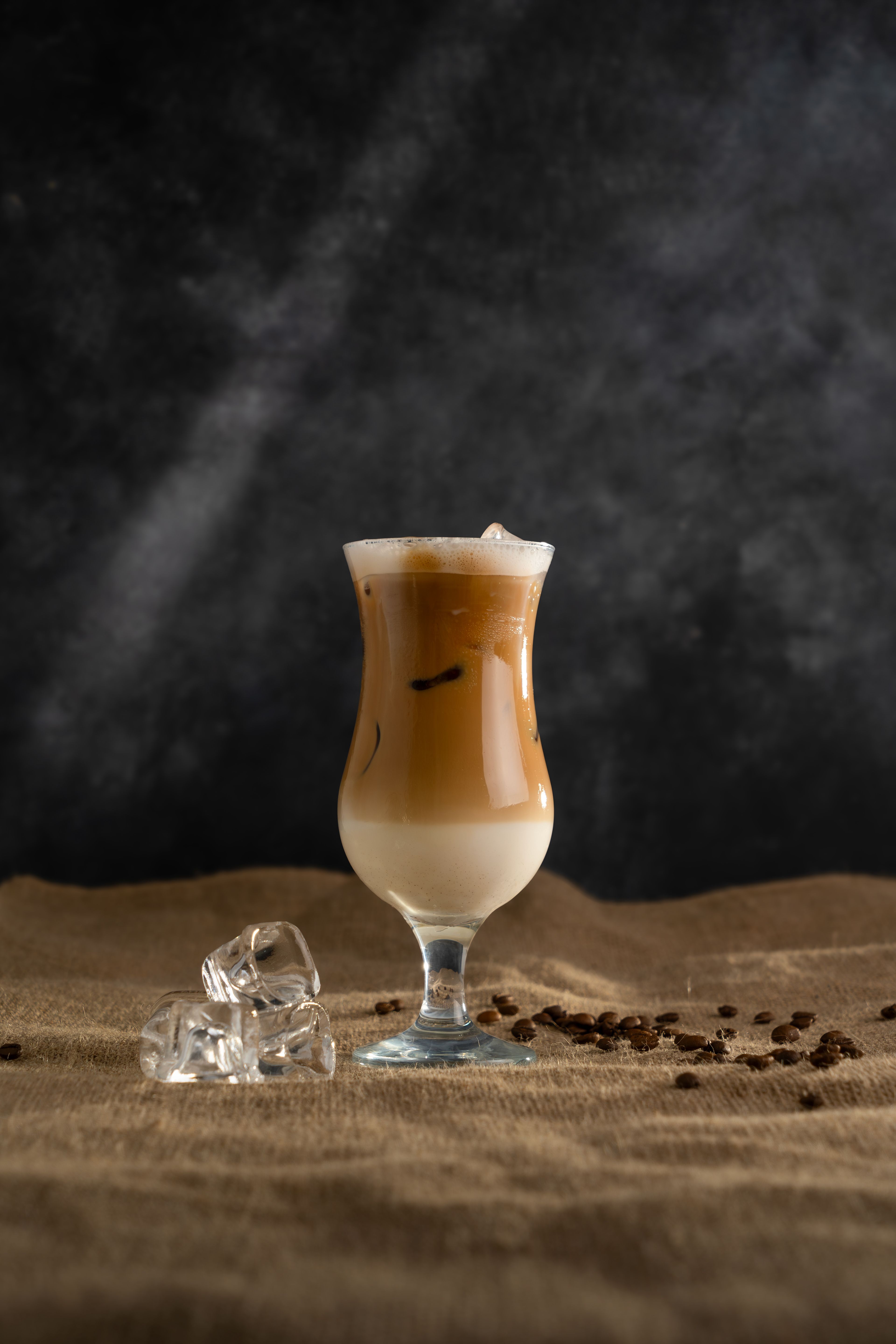 Aesthetic iced coffee latte with ice cubes and coffee beans on a textured surface.