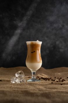 Aesthetic iced coffee latte with ice cubes and coffee beans on a textured surface.