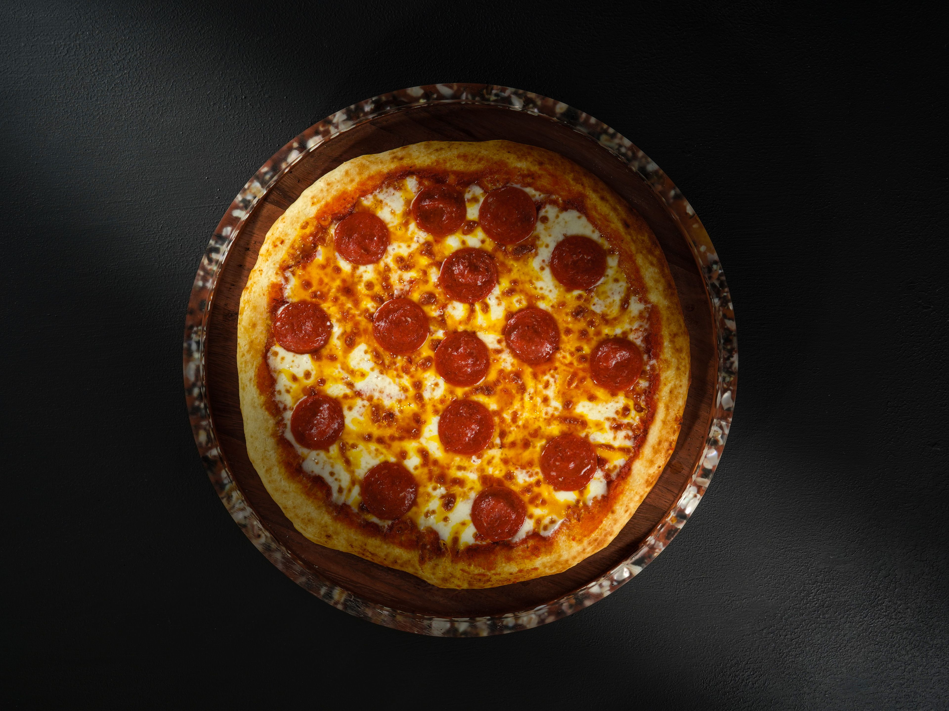a hand lifting one slice from a whole pepperoni pizza with a long molten cheese pull, lit by warm amber neon glow against a dark green wall