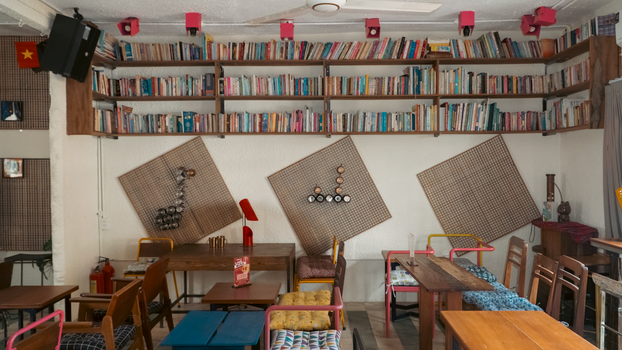 A cozy cafe featuring shelves filled with books, colorful chairs, and a warm atmosphere.