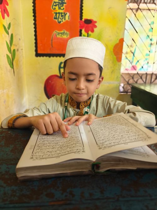 Free A young boy wearing traditional clothing reads a book in a colorful classroom setting. Stock Photo
