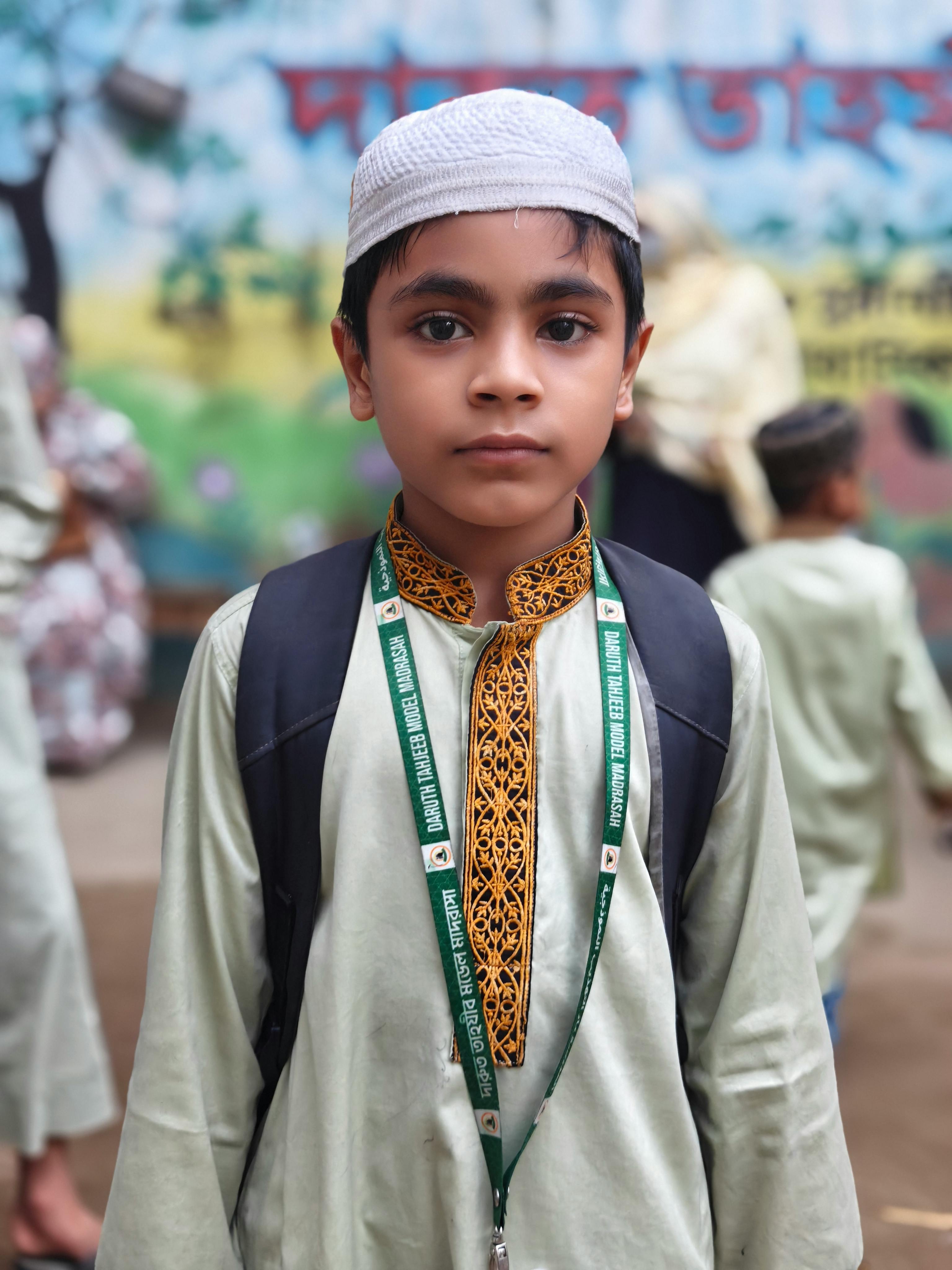Portrait of a young boy wearing traditional attire and a backpack, standing outdoors with a blurred background.