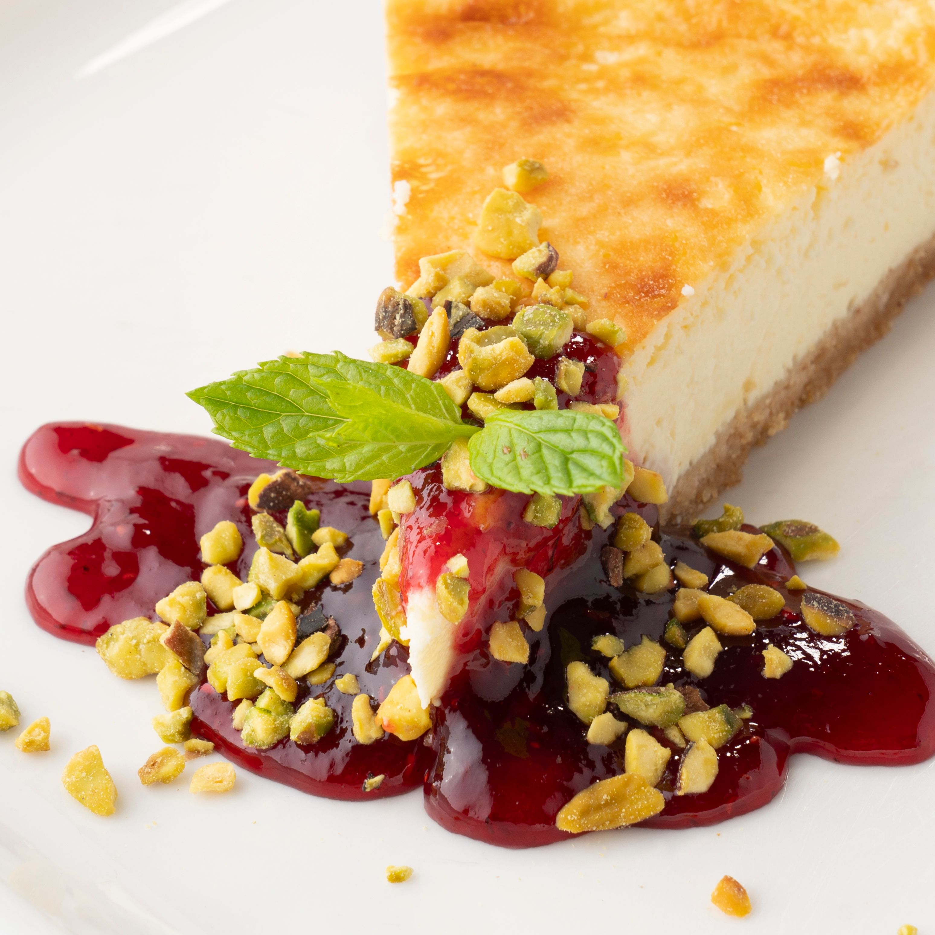 A delectable slice of cheesecake with raspberry sauce and pistachios, perfect for dessert lovers.