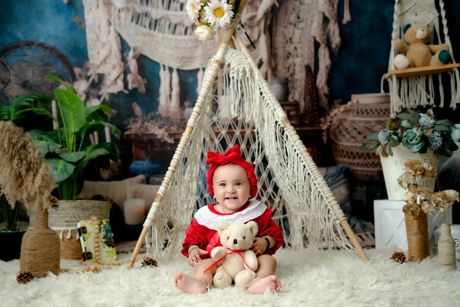 Charming baby in red outfit with teddy bear inside a decorative indoor teepee.