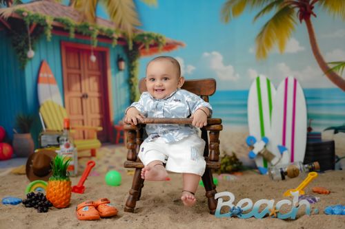 Free Adorable baby in summer beach-themed setup, surrounded by playful beach toys, tropical decor, and surfboards. Stock Photo