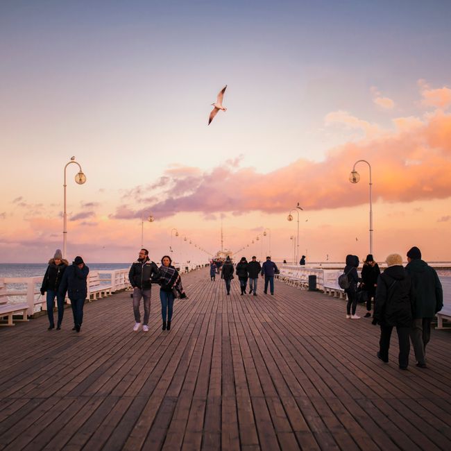 People walking on Sopot Pier during a vibrant sunset, capturing a serene seaside atmosphere.