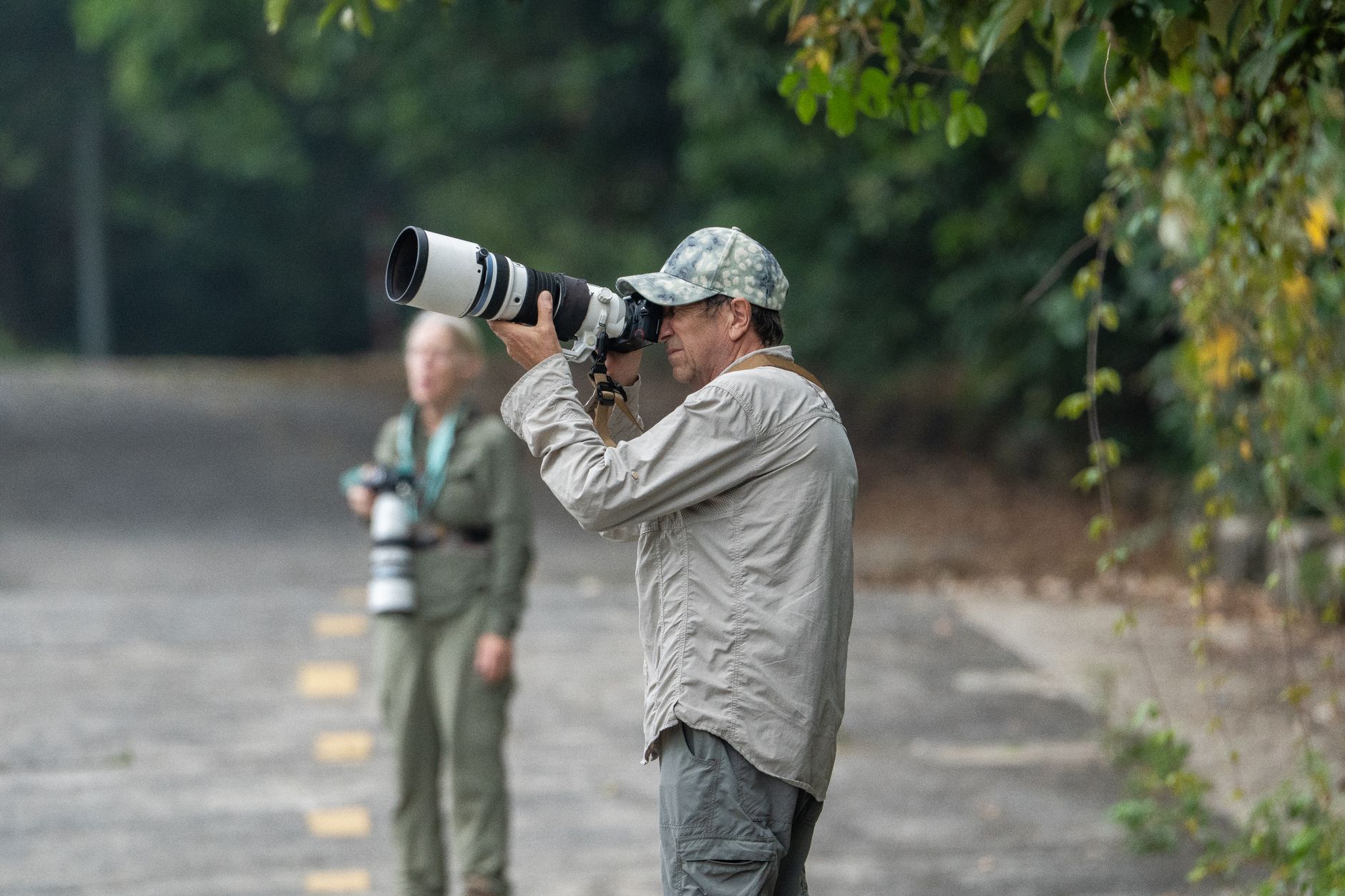 Two wildlife photographers capturing nature scenes with telephoto lenses, standing on a path.