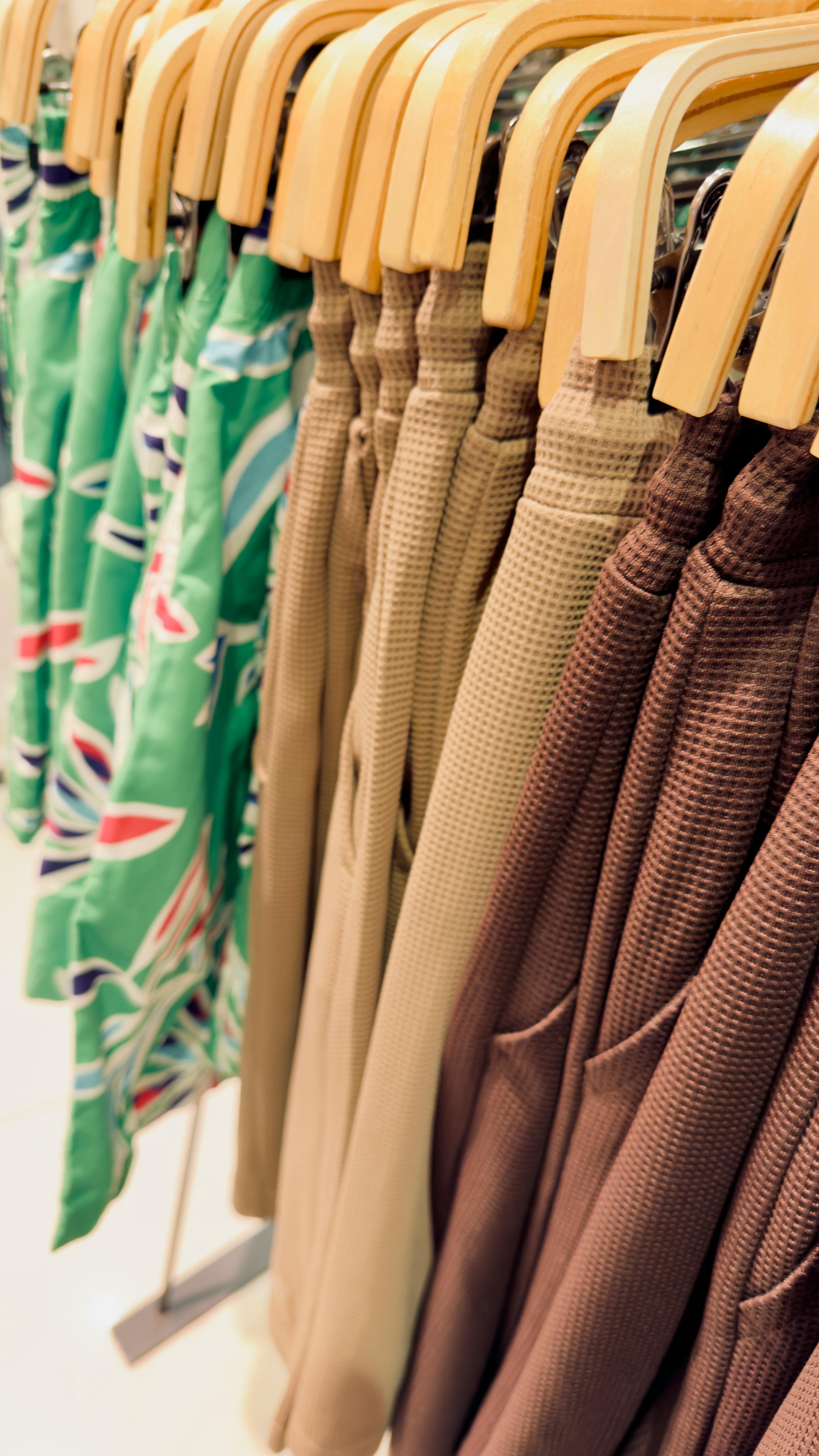 Browse a vibrant display of summer clothes on wooden hangers, featuring textures and patterns.