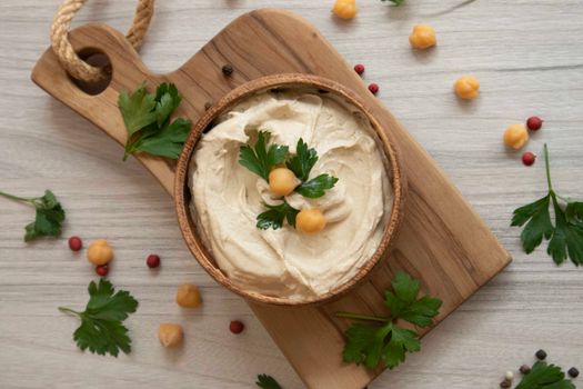 Creamy hummus garnished with chickpeas and parsley on a rustic cutting board. Perfect for food presentations.
