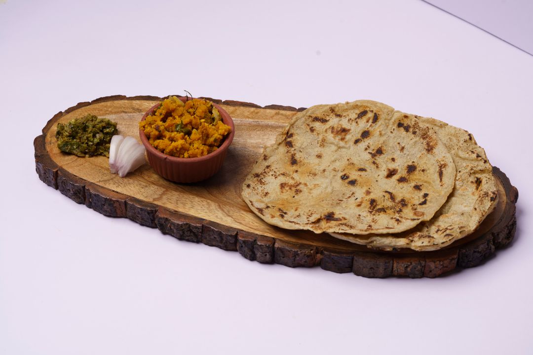 Kathiyawadi Cuisine: Gujarat's Boldest Regional Food Tradition Explained 3 A rustic wooden platter of Kathiyawadi cuisine with hand-patted flatbreads, a bowl of spiced yellow sabzi, green chutney and raw onion