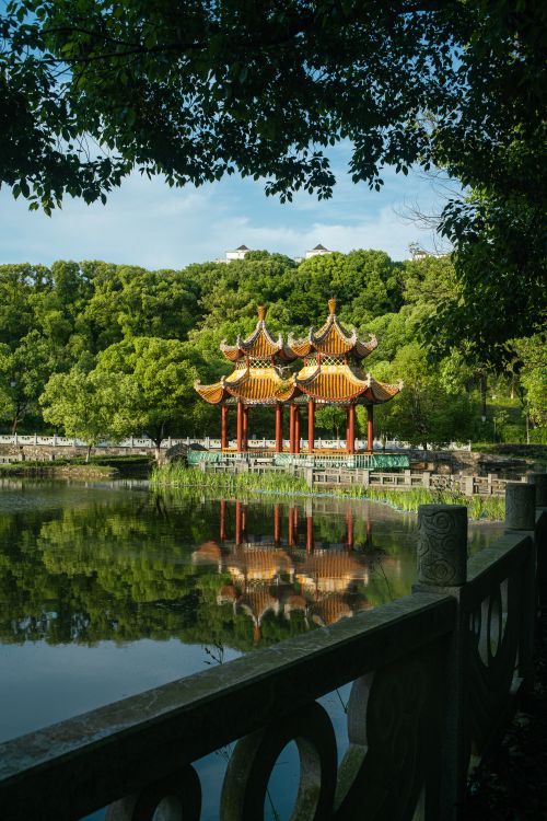 Free A scenic view of a Chinese pavilion reflected in a tranquil lake surrounded by lush greenery. Stock Photo