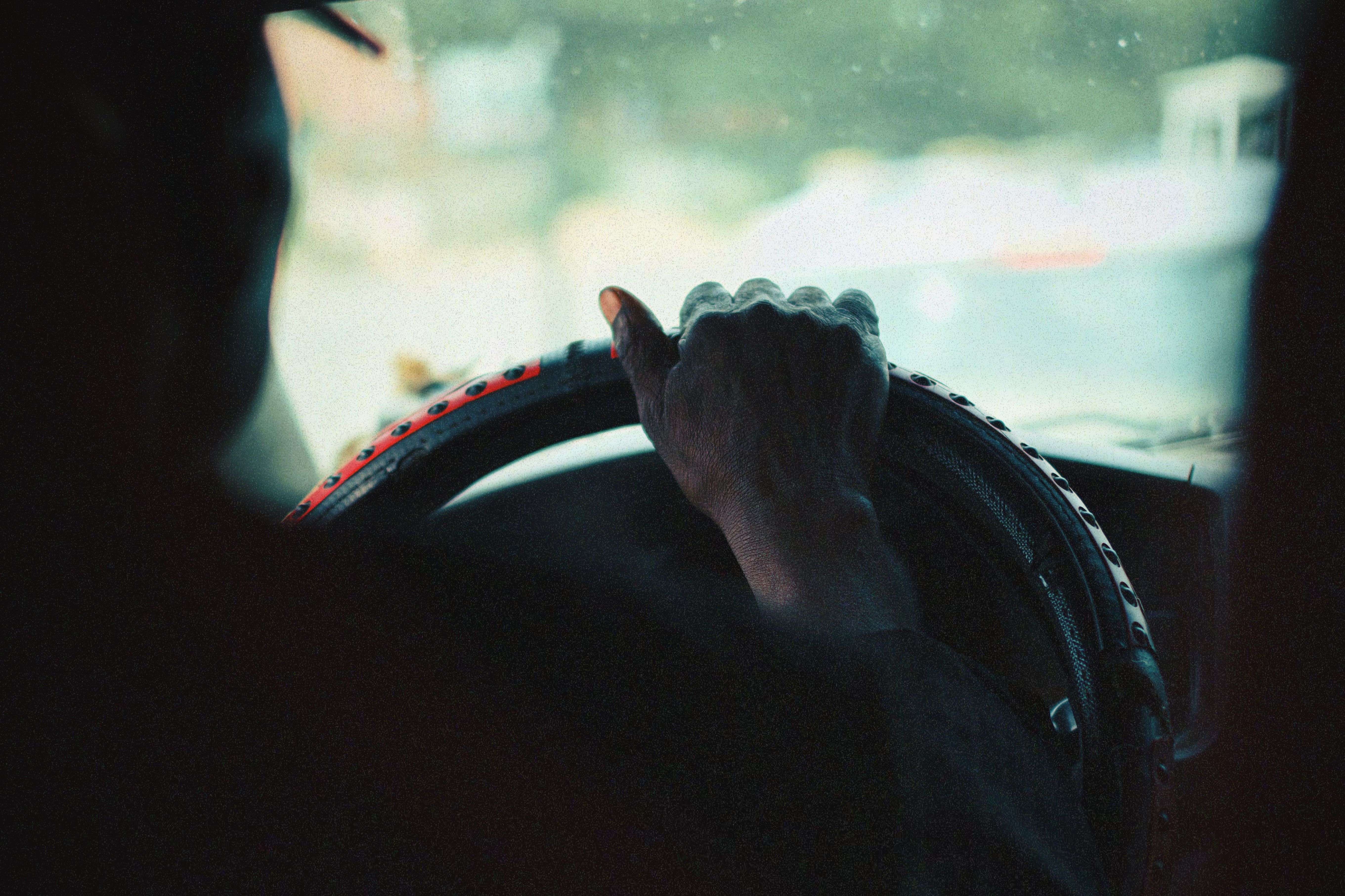 A close-up view of a person's hand gripping a car steering wheel, captured with a vintage aesthetic.