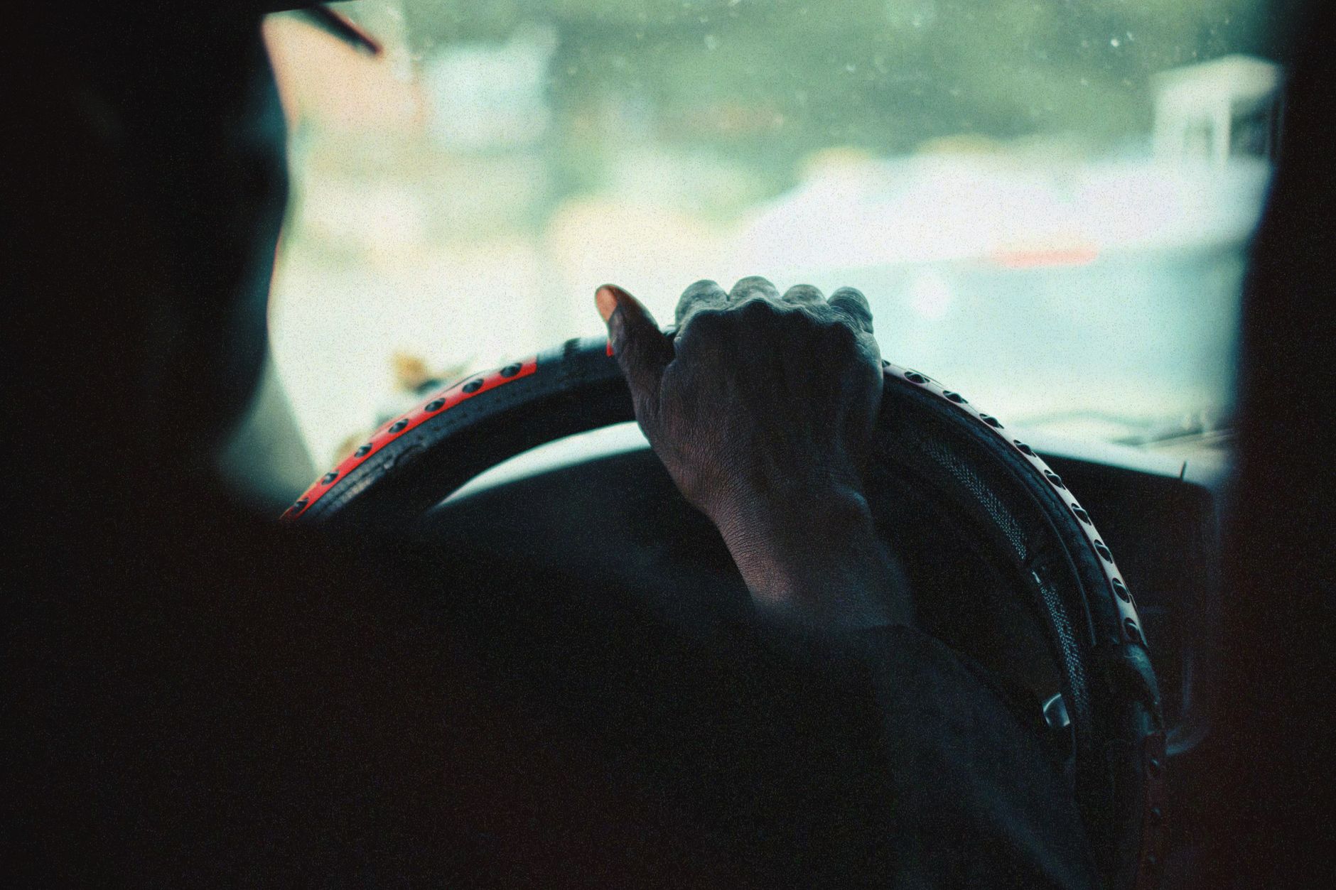 A close-up view of a person's hand gripping a car steering wheel, captured with a vintage aesthetic.