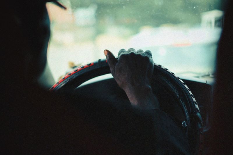 A close-up view of a person's hand gripping a car steering wheel, captured with a vintage aesthetic.