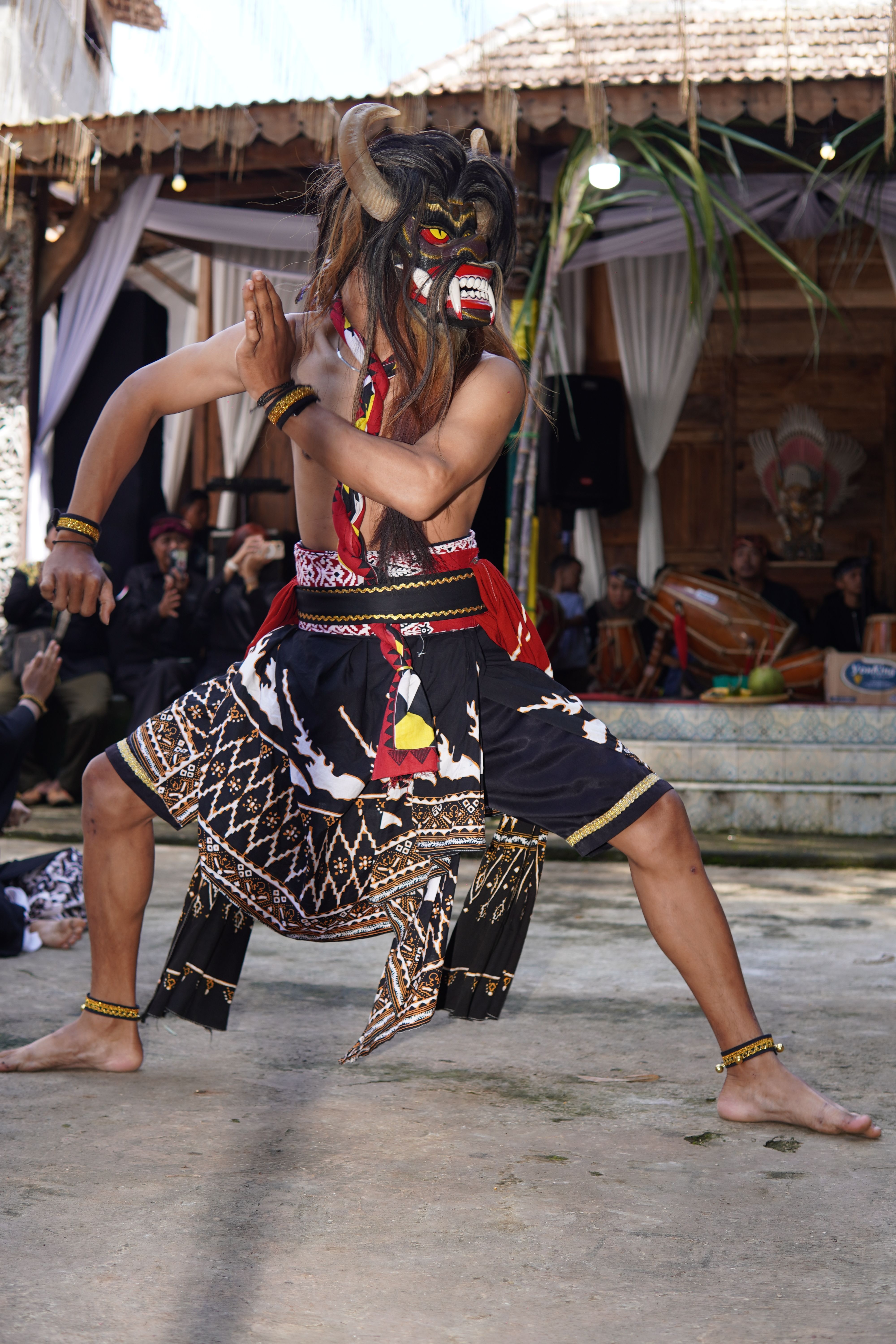 A cultural dance performance featuring a dancer in traditional Indonesian attire and mask.