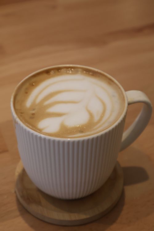 Free A detailed shot of a latte with beautiful milk foam art in a ribbed white mug on a wooden table. Stock Photo