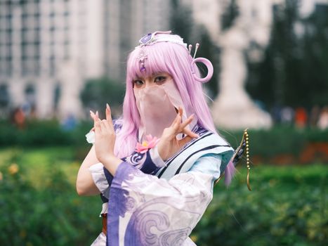 Cosplay enthusiast poses in colorful attire with lavender hair outdoors in Vietnam.