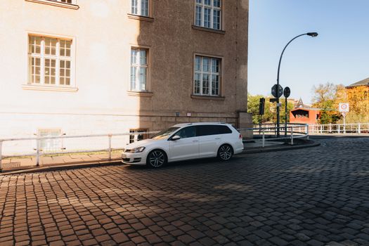 A quiet city road in Berlin with a white car parked, capturing warm sunlight and urban architecture.