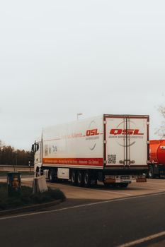 A white delivery truck travels on an urban road in Berlin, Germany, under a moody sky.