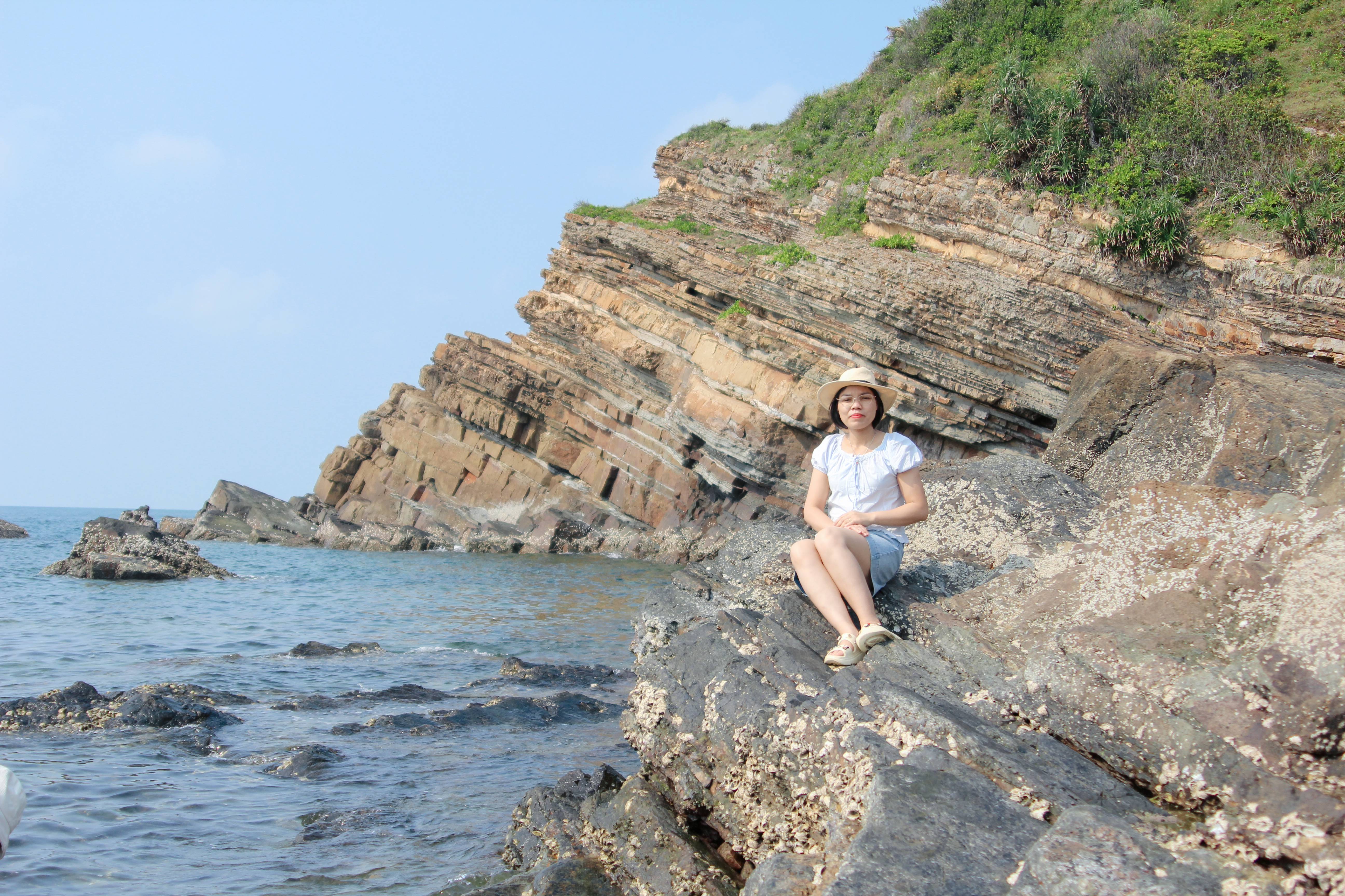 Woman sitting on rocky beach against scenic cliff with ocean view.