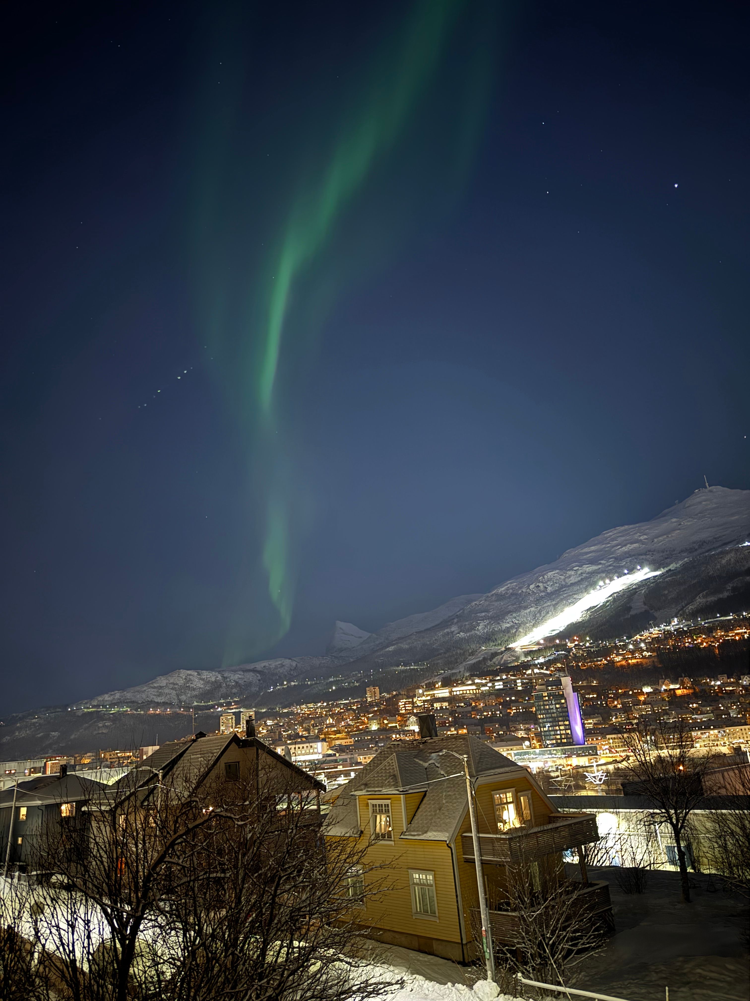 Green aurora over the lit rooftops of Tromso on a clear winter night.