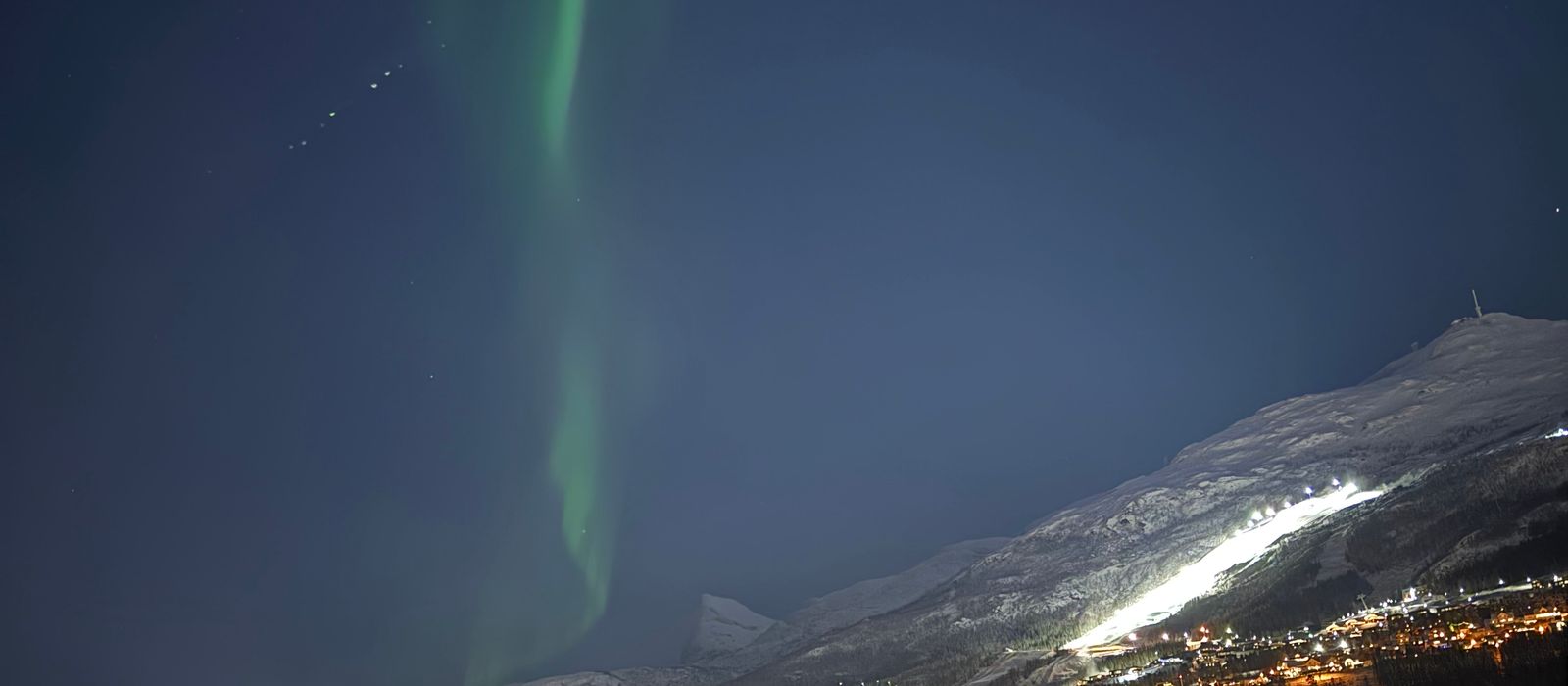 Green aurora over the lit rooftops of Tromso on a clear winter night.