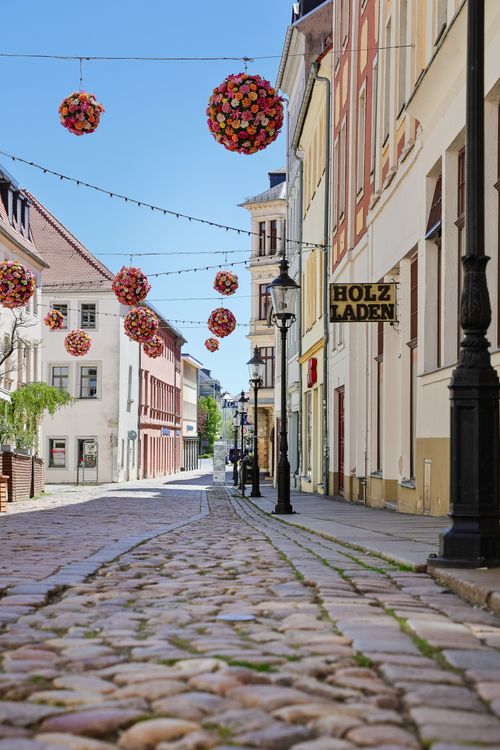 Free Charming street view in Freiberg, Germany with floral decorations hanging above cobblestone pavement. Stock Photo