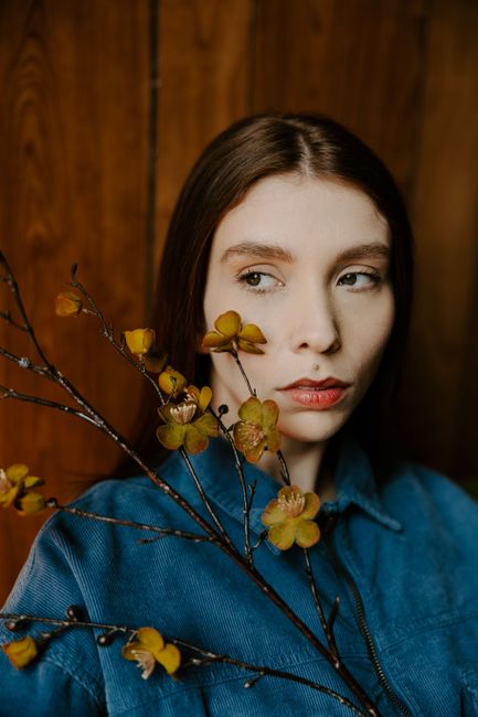 Artistic portrait of a woman with yellow flowers against a wooden background, exuding a vintage vibe.