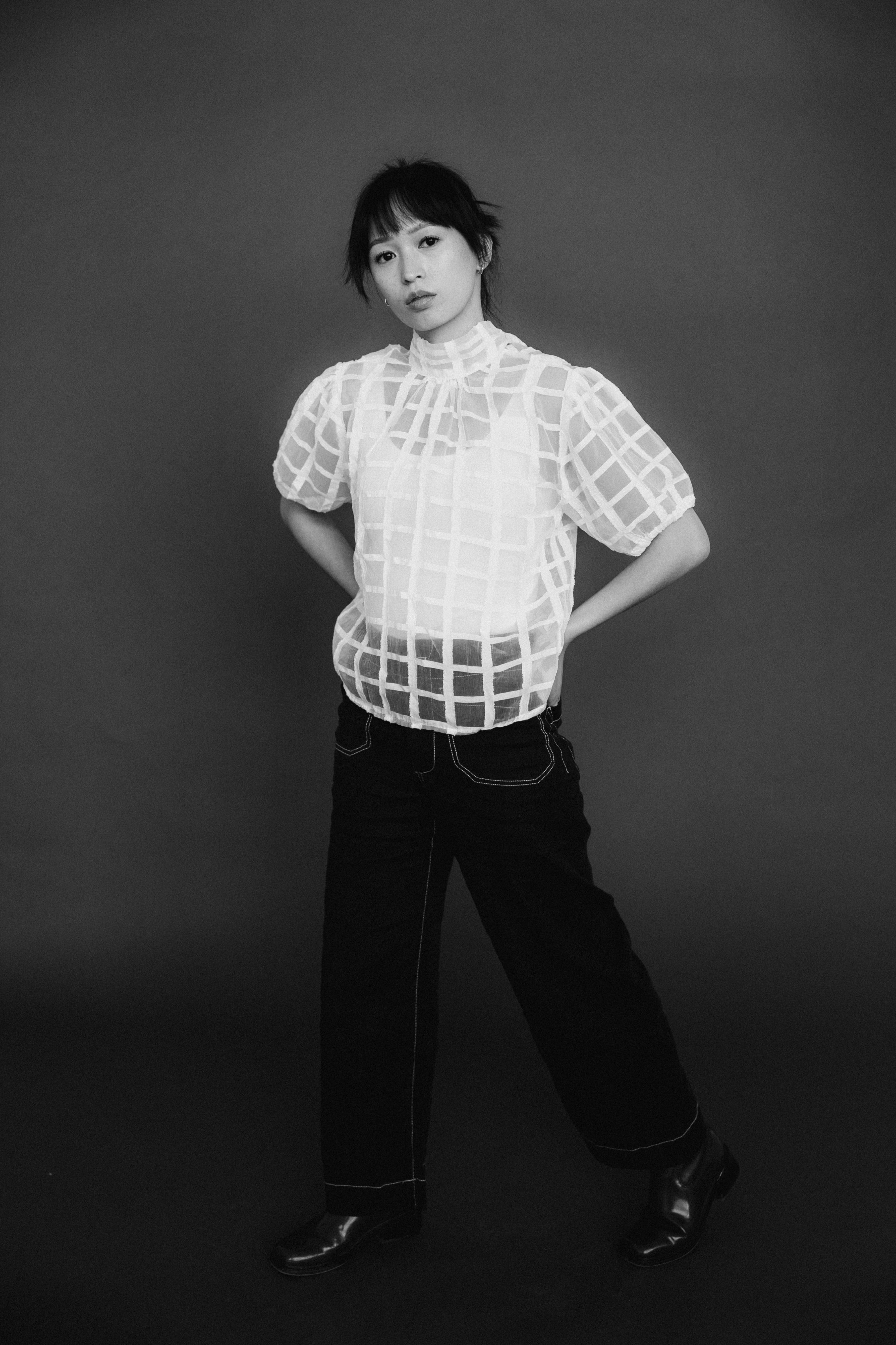 Black and white portrait of a young model in a stylish outfit, exuding modern fashion elegance in a studio setting.