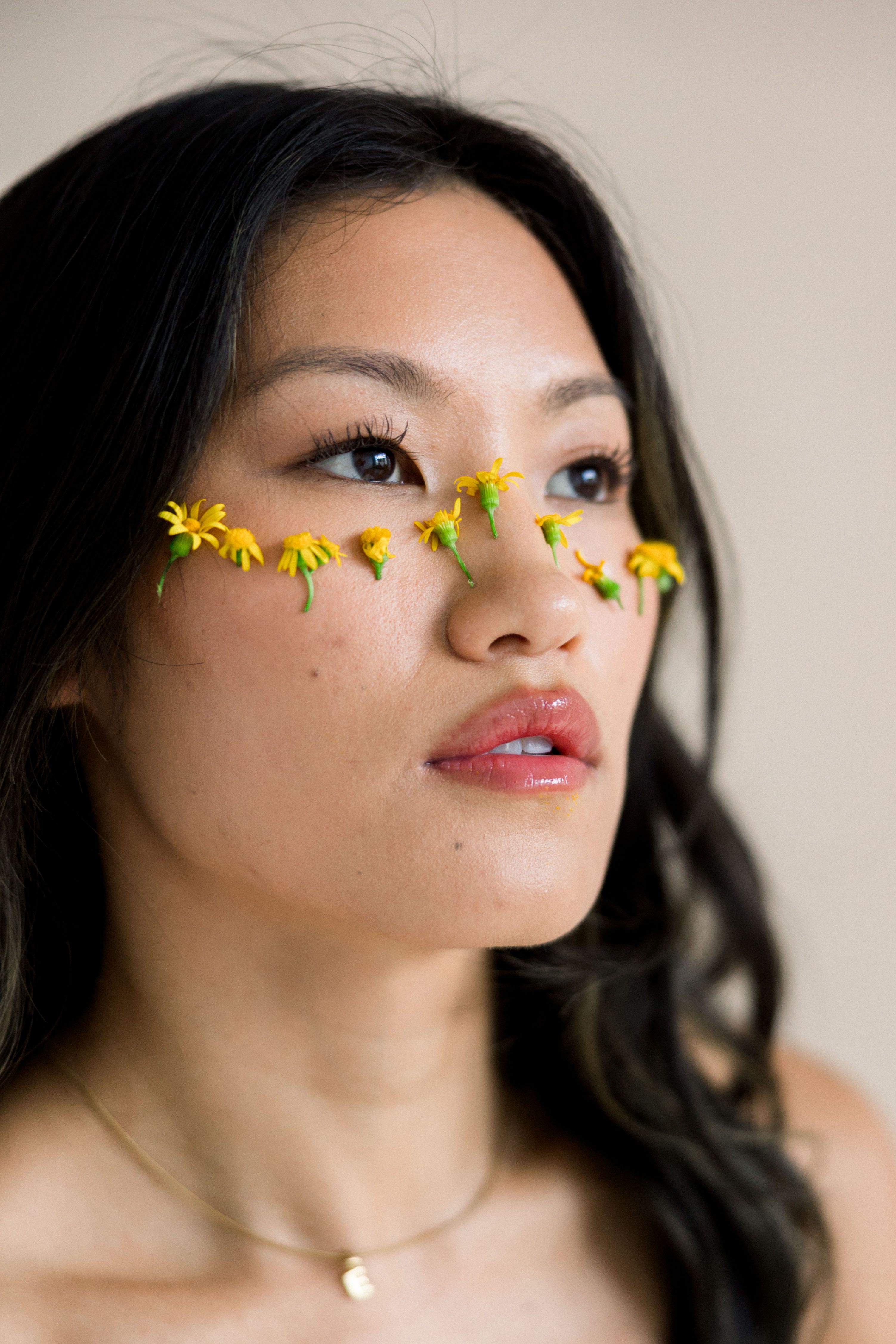 Artistic portrait of a woman with yellow flowers accentuating her eyes against a soft background.