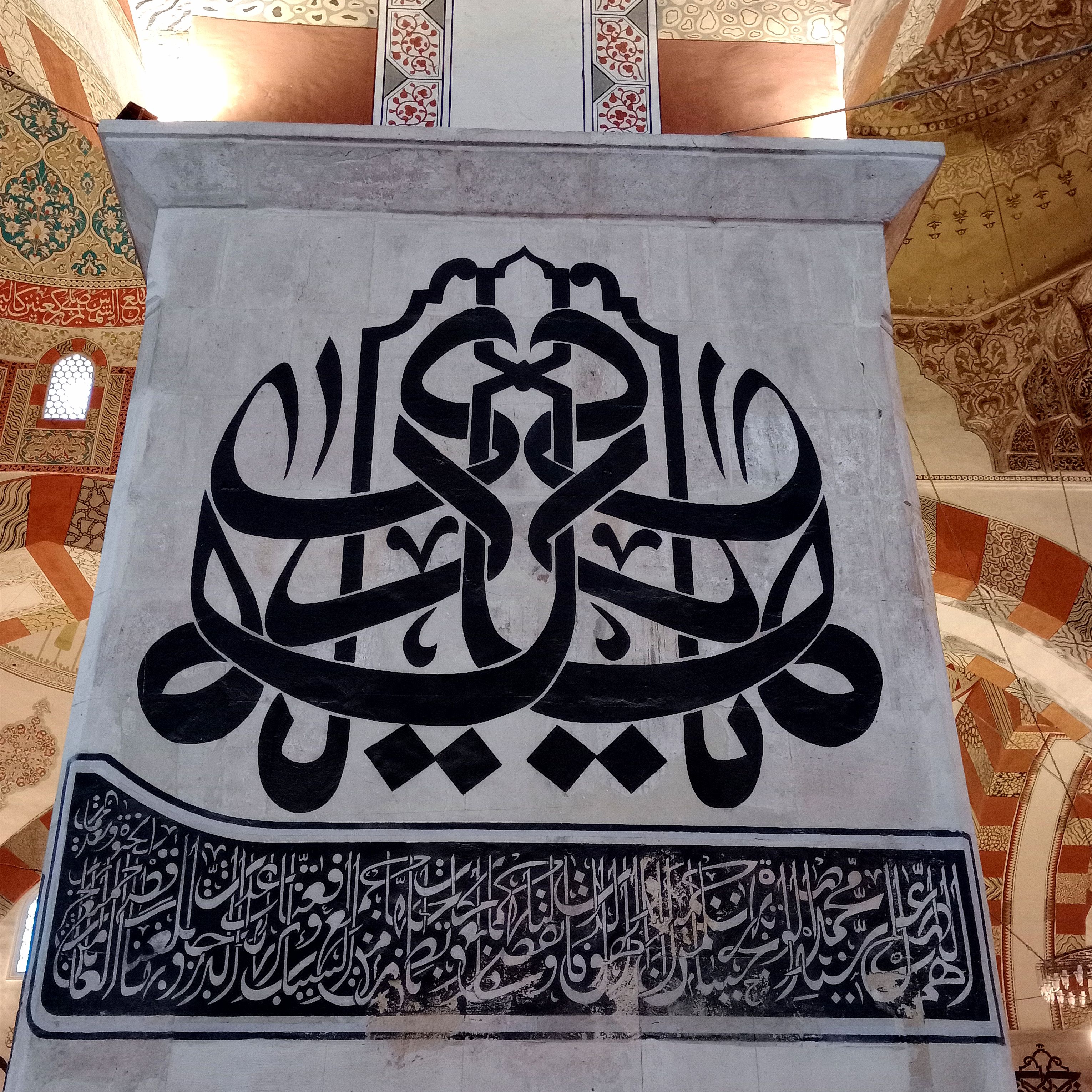 Detailed Arabic calligraphy on a mosque interior wall showcasing Islamic art style.