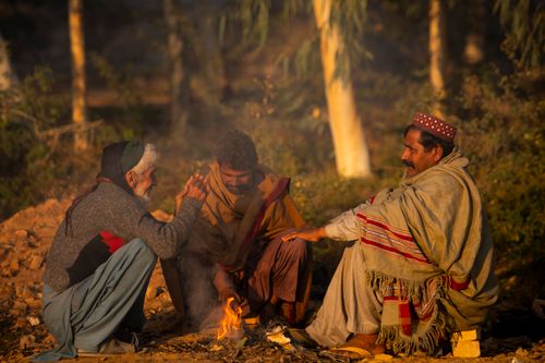 Free Three Pakistani farmers sitting by a fire in a rural setting, enjoying a warm conversation. Stock Photo