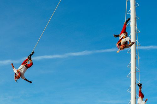 Free Colorful Mexican voladores ceremony with performers descending from a tall pole against a blue sky. Stock Photo